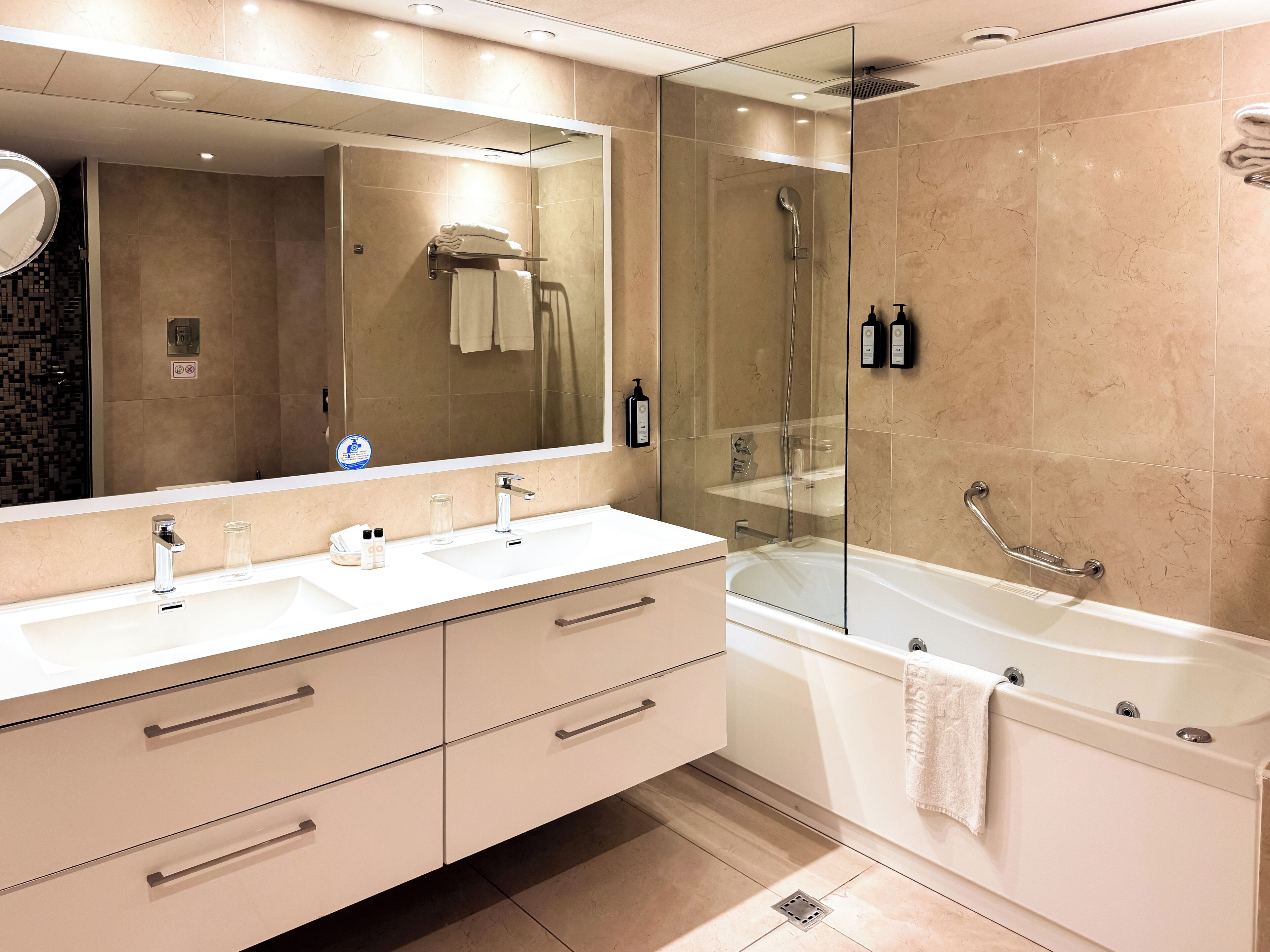 Un baño moderno con ducha de vidrio, un espejo grande y un mueble de tocador blanco con cajones.