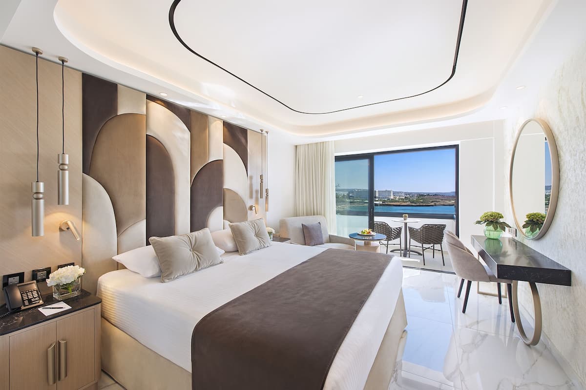 A modern hotel room with a large bed, a desk, and a view of the city.