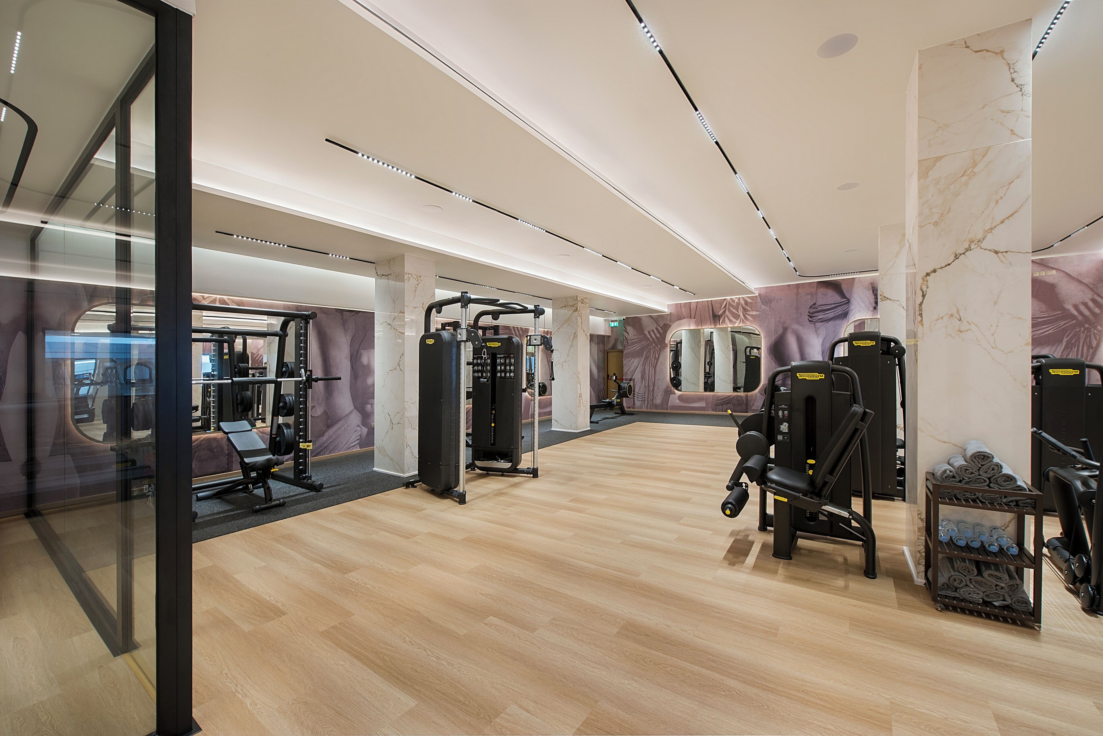 Une salle de sport moderne équipée de divers appareils d’exercice, avec des murs en marbre et un plancher en bois.