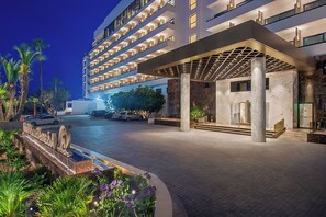 A modern hotel entrance with a covered walkway, palm trees, and a well-lit driveway.