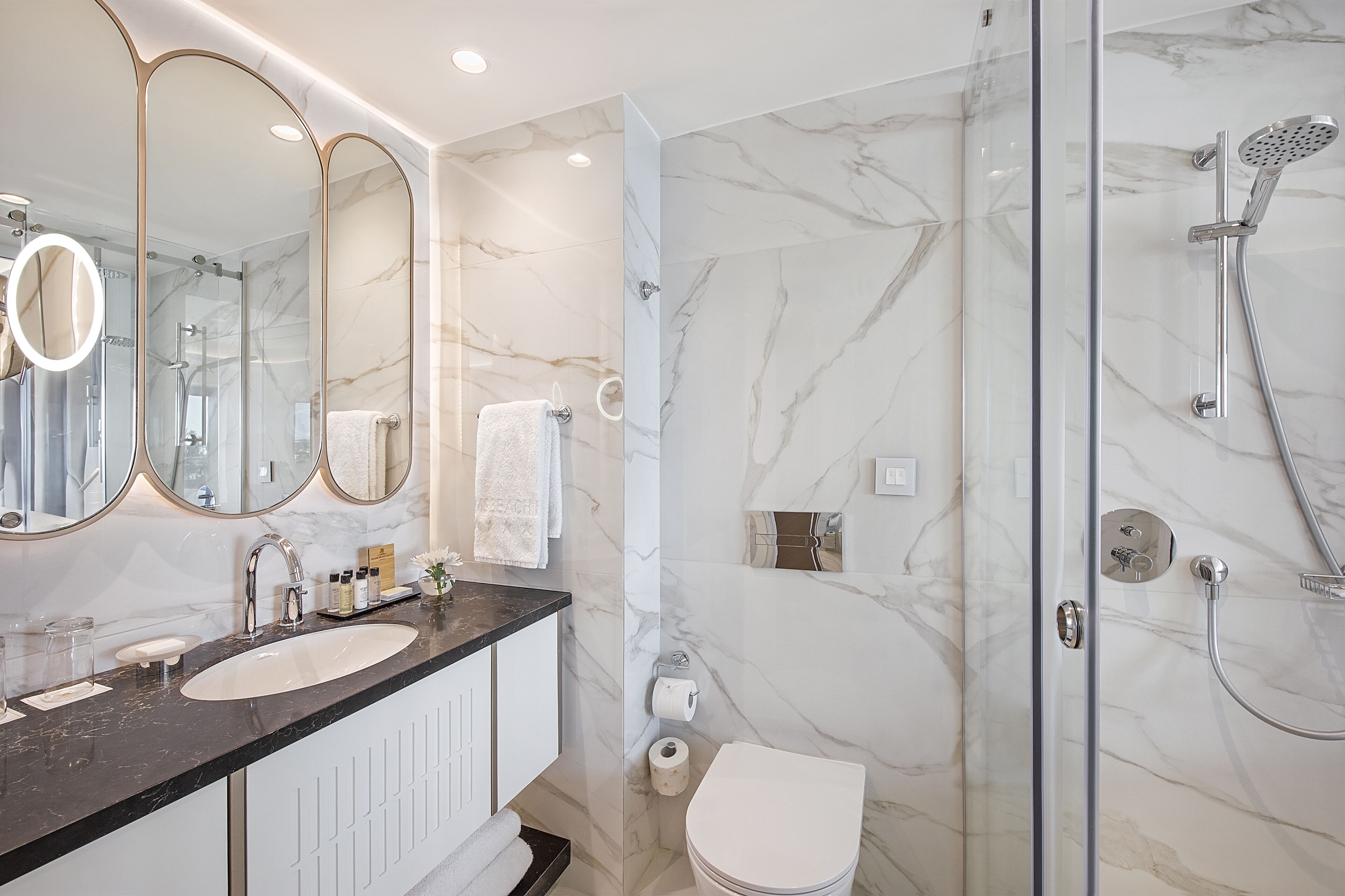 A modern bathroom with two sinks, a glass-enclosed shower, and marble walls.