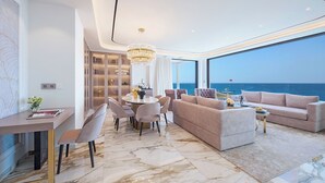 A modern living room with a marble floor, a round dining table with chairs, a sofa, and a large window overlooking the sea. - Adams Beach Hotel & Spa (Ayia Napa)