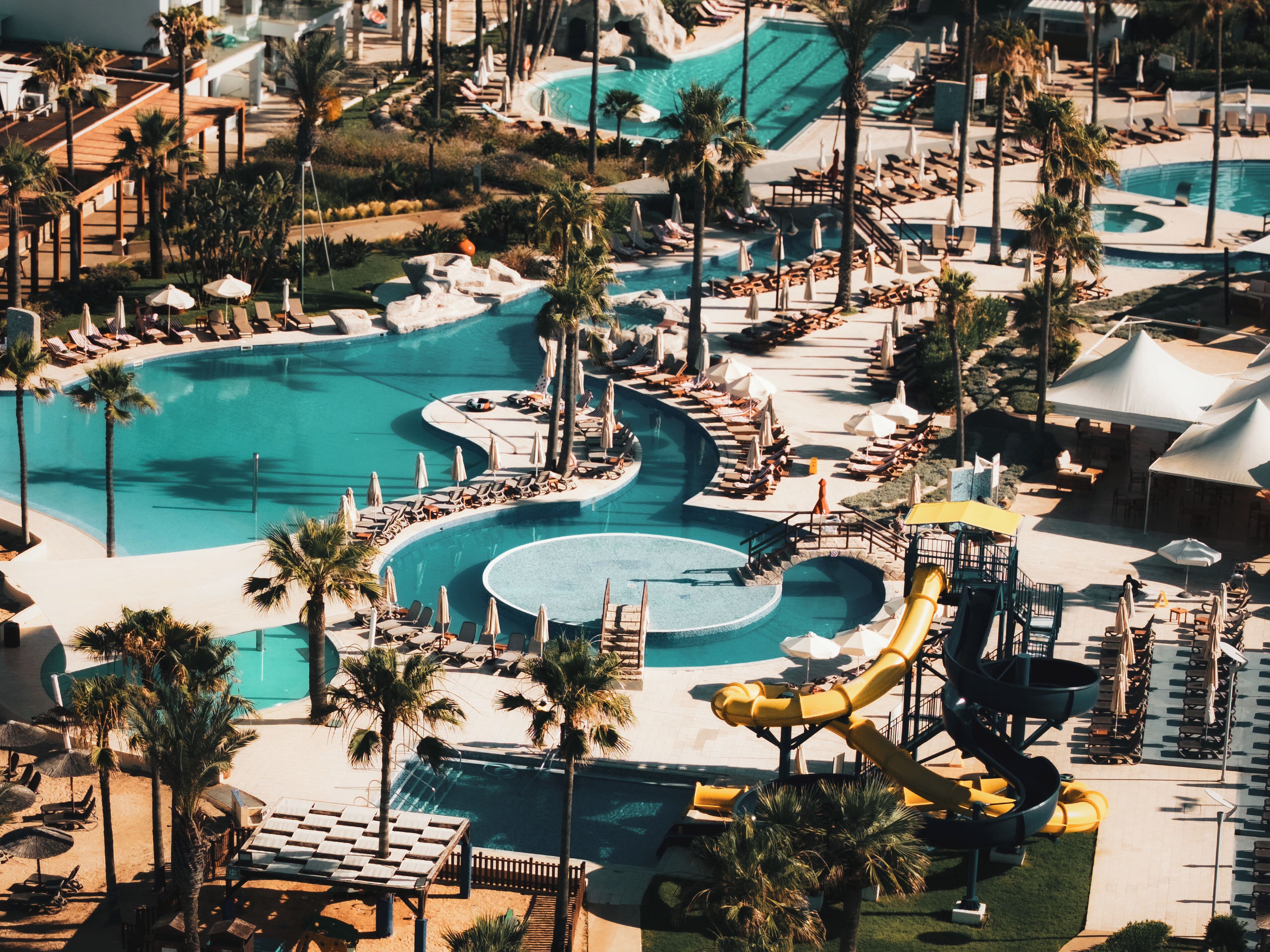 A resort with multiple swimming pools, sun loungers, and palm trees.