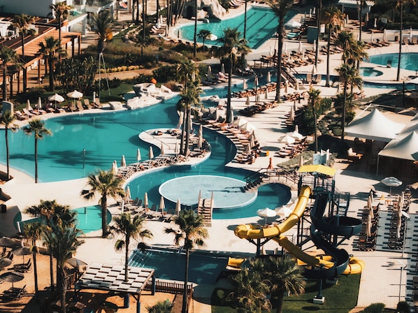Un resort con varias piscinas, tumbonas y palmeras.