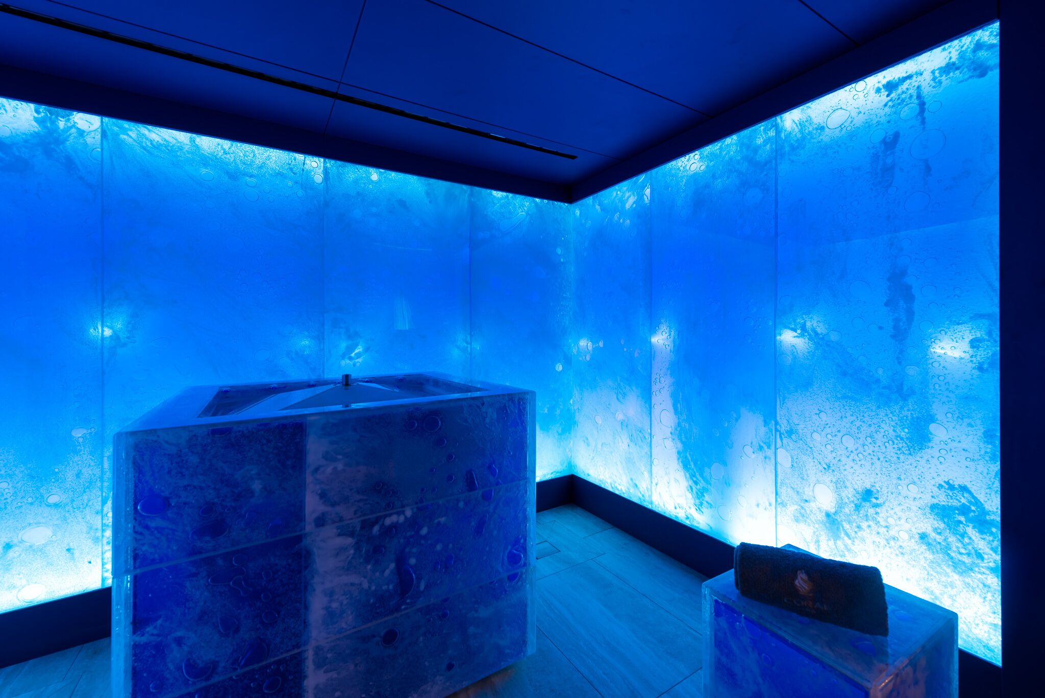 Ein Zimmer mit einer großen Glaswand, die eine Unterwasserlandschaft zeigt, Holzboden und einer transparenten Glasbaustruktur.