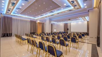 Un salón de conferencias con filas de sillas, una pantalla de proyector y una pantalla grande.