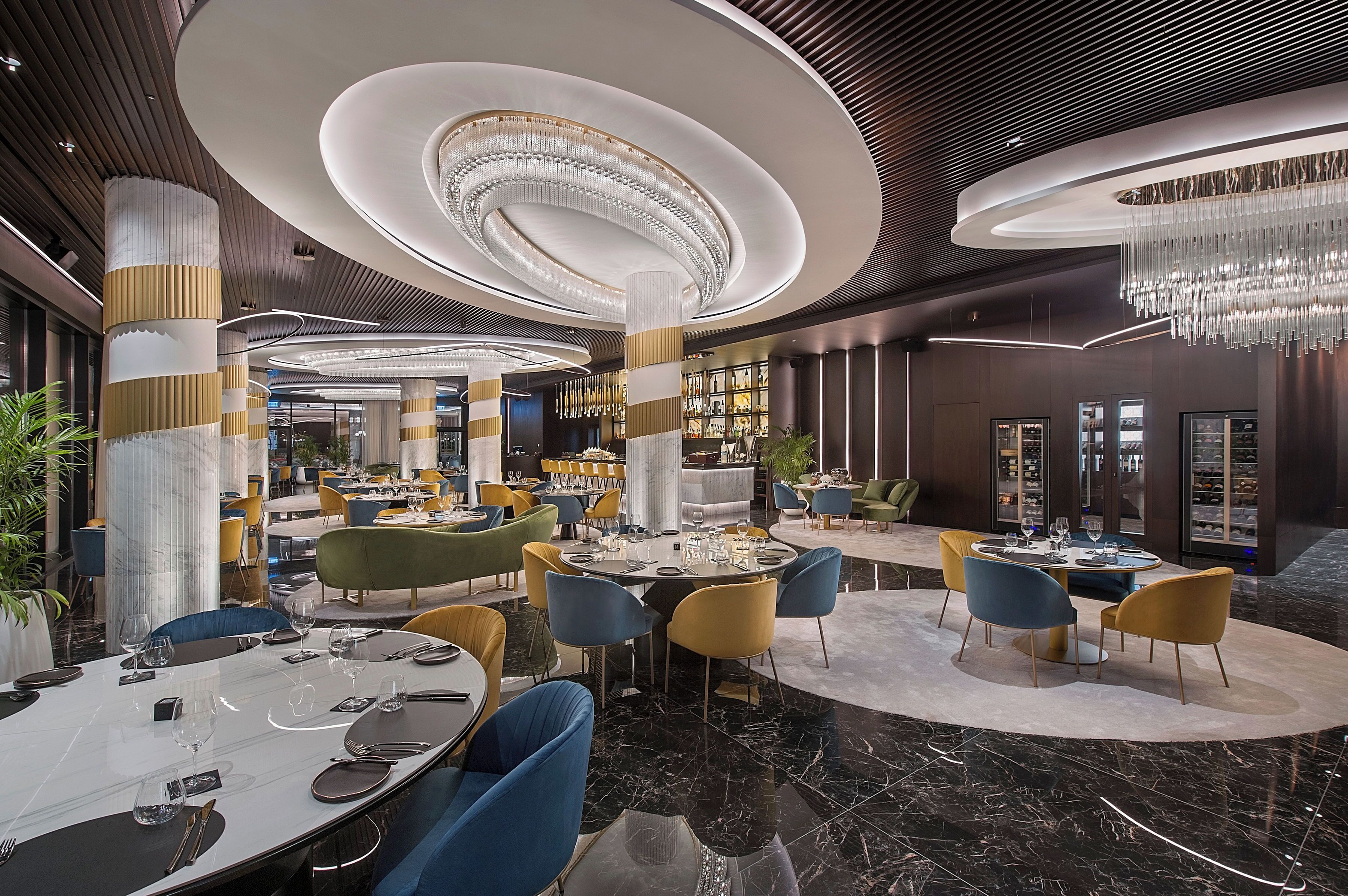 A modern hotel lobby with circular seating areas, a central column, and a chandelier.