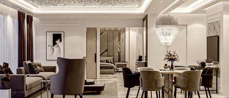 A modern, well-lit living room with a sofa, armchairs, and a dining area with a chandelier.