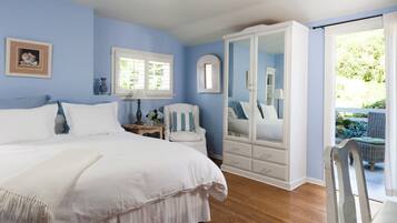 A bedroom with a large bed, a white wardrobe, a chair, and a window with a view of greenery outside.