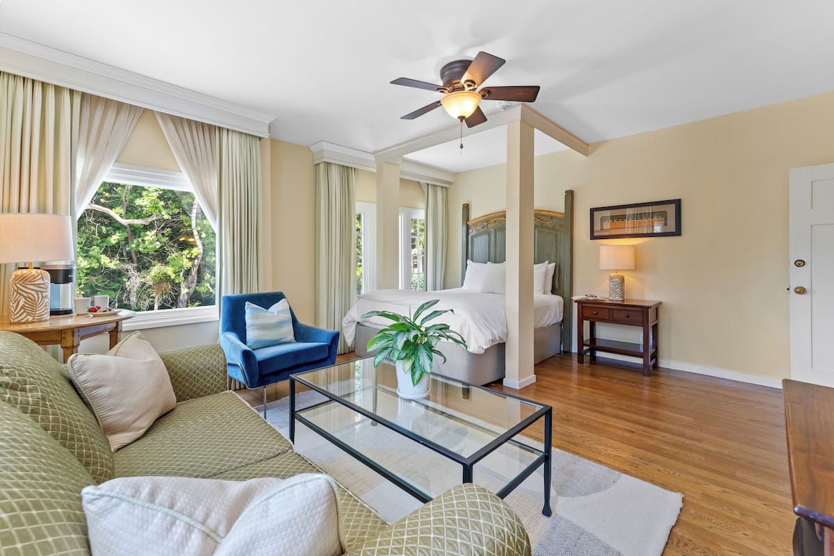 A well-lit room with a bed, a blue chair, a glass coffee table, and a ceiling fan.