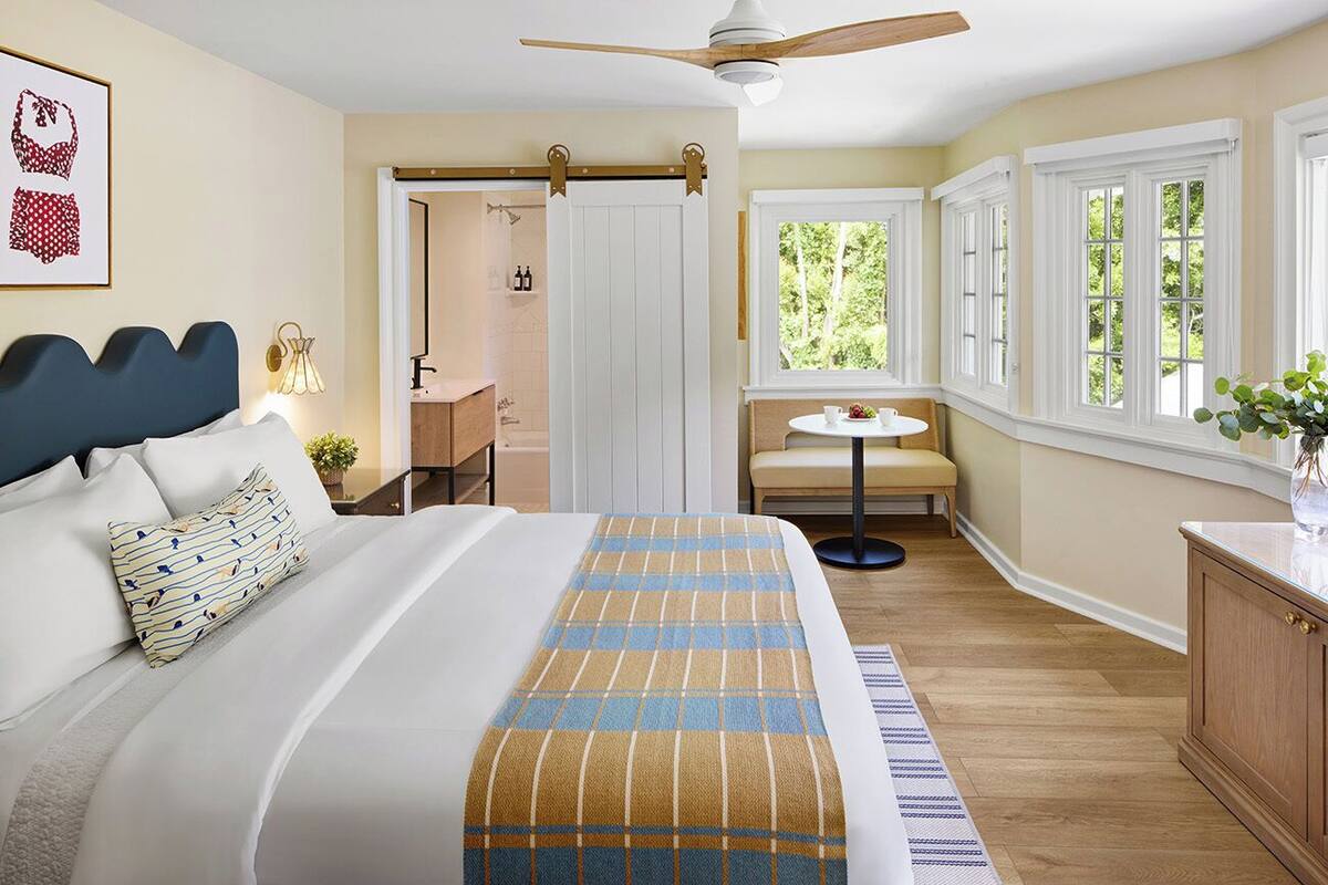 A bedroom with a bed, bedside table, and a window with a view of greenery.