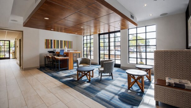 A spacious lobby with a wooden ceiling, large windows, a reception desk, and seating areas.