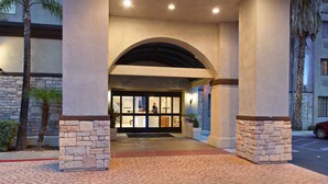 A hotel entrance with a stone facade, an arched doorway, and a palm tree to the left.