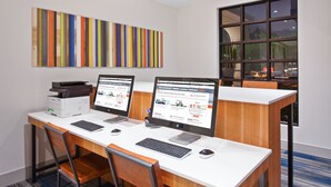 A modern office with two desktop computers, a printer, and a large window with a view of palm trees.