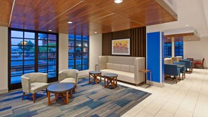 A spacious lobby with a large seating area, a sofa, and a coffee table. There are large windows offering a view of the outside.