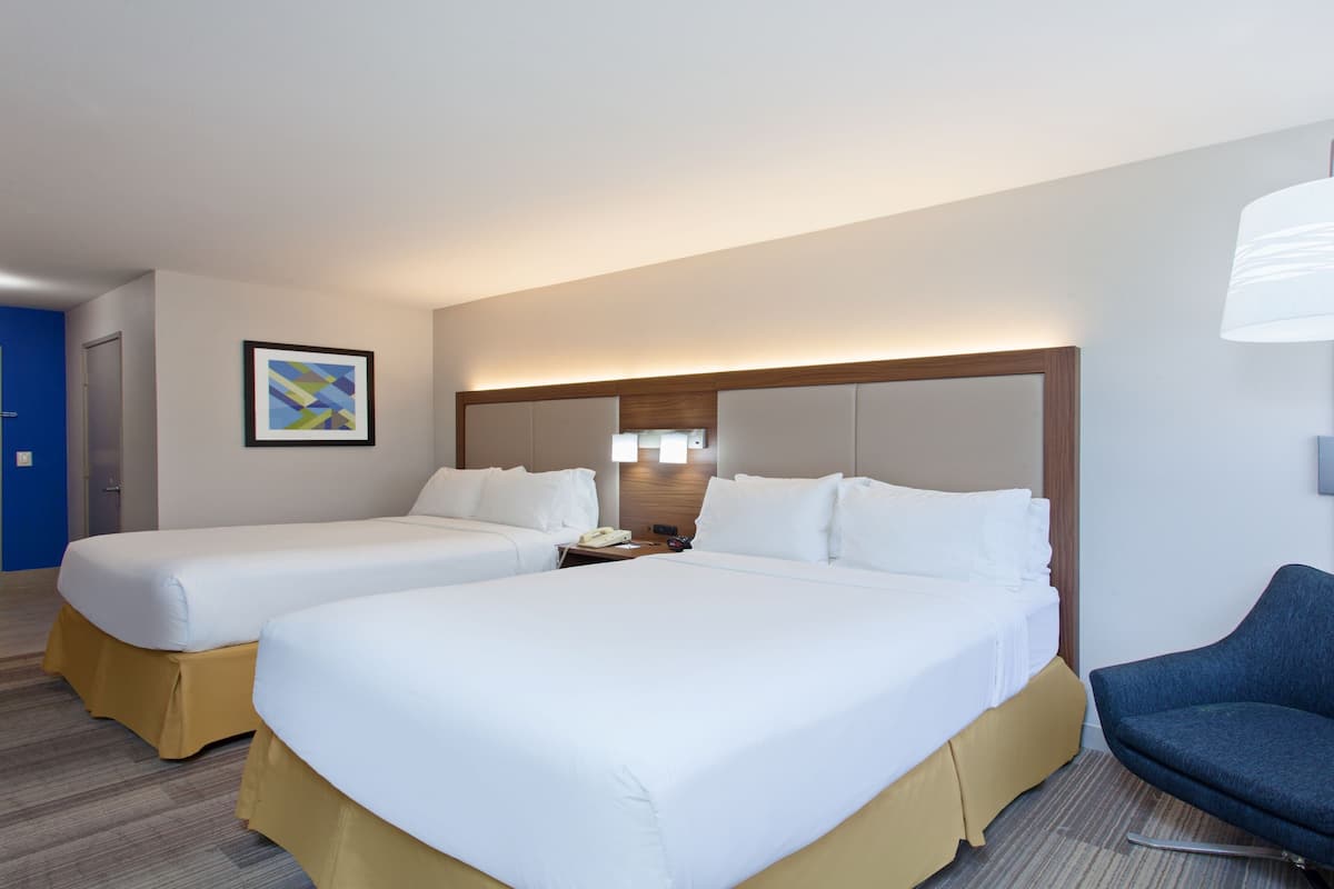 Une chambre d’hôtel avec deux lits, un bureau, une chaise, une lampe et un tableau au mur.