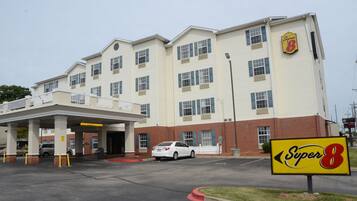 A Super 8 hotel with a two-story building, a covered parking area, and a white car parked in front.