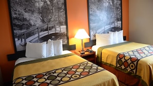 Quarto de hotel com duas camas, cada uma com colcha estampada, uma mesa de cabeceira com abajur, e duas fotos emolduradas na parede.