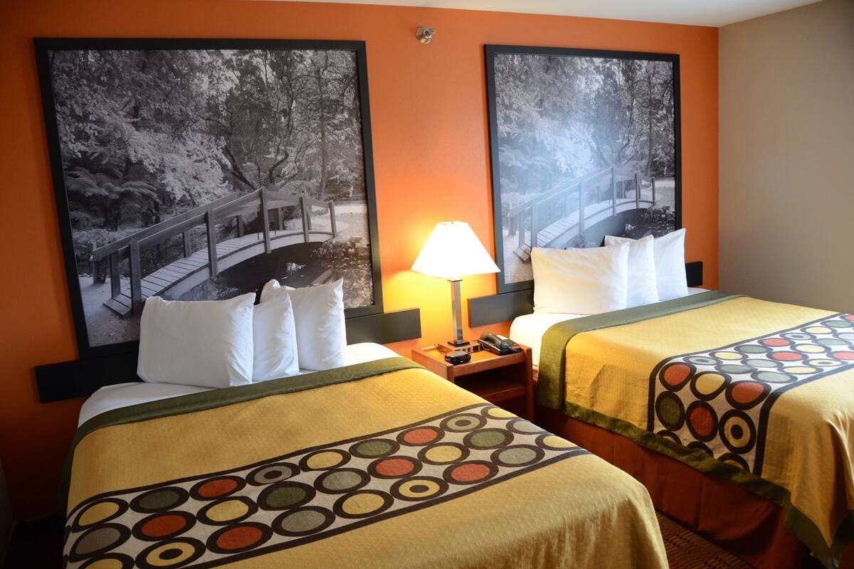 A hotel room with two beds, each with a patterned bedspread, a nightstand with a lamp, and two framed pictures on the wall.