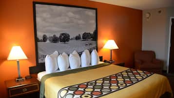 Habitación de hotel con una cama grande, dos lámparas de noche, una silla y un cuadro con un paisaje en la pared.