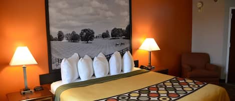 Habitación de hotel con una cama grande, dos lámparas de noche, una silla y un cuadro con un paisaje en la pared.