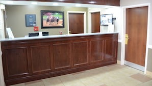 Uma área de recepção com um balcão de madeira, um quadro com cavalos, um alarme de incêndio e uma câmera de segurança.