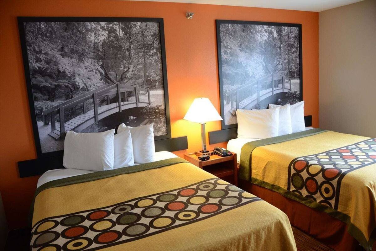 A hotel room with two beds, each with a patterned bedspread, a nightstand with a lamp, and two framed pictures on the wall.