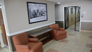 Um hall com dois poltronas laranja, um banco de mármore e um letreiro de boas-vindas emoldurado.
