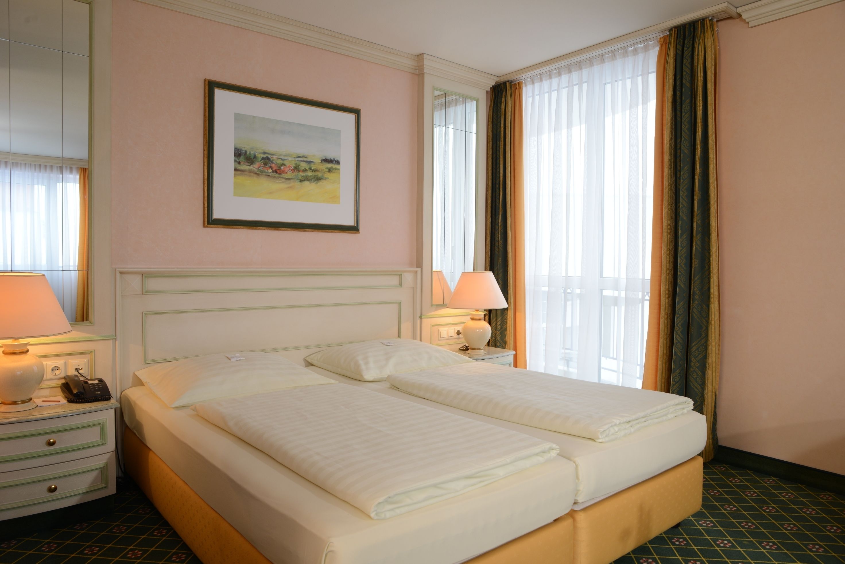 A double bed with white linens, a bedside table with a lamp, a framed picture on the wall, and a window with curtains.