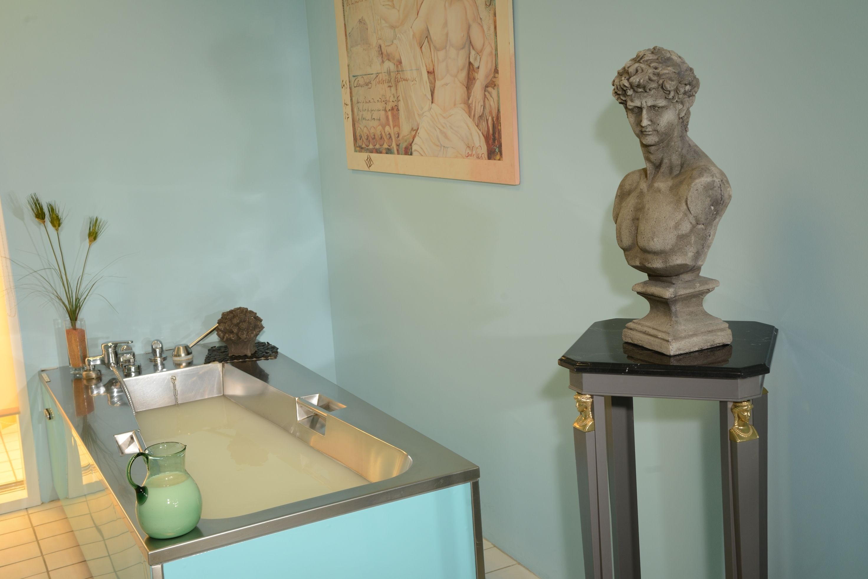 A bathroom with a bathtub, a sink, and a marble sculpture on a pedestal.
