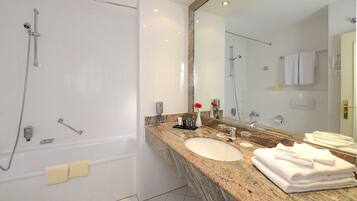 Un baño moderno con bañera, ducha, lavamanos con encimera de granito y un espejo grande.