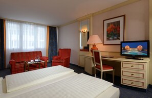A hotel room with a bed, a desk with a computer, a TV, a chair, and a sofa. - The Monarch Hotel (Neustadt an der Donau)