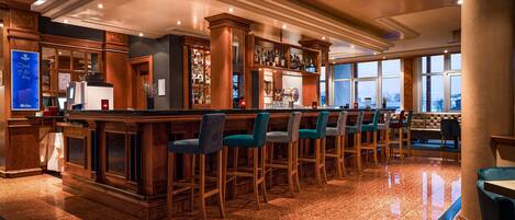 Zona de bar con mostradores de madera, varios taburetes y un área de estar con sofá y sillones.