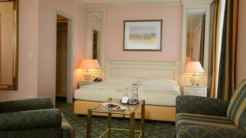 A hotel room with a bed, two bedside tables with lamps, a small table with a plate of food, and two patterned armchairs.
