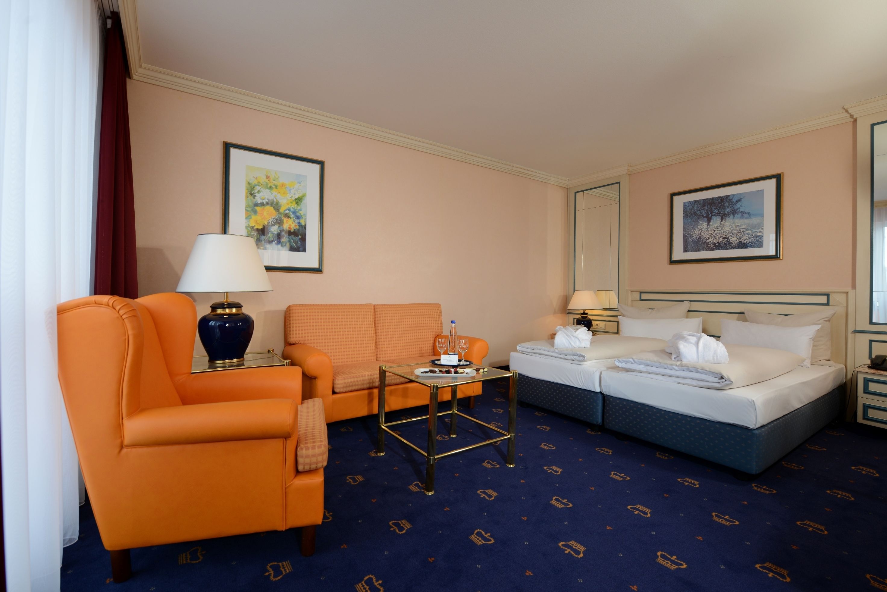 A hotel room with an orange armchair, a sofa, a bed, a small table, and a nightstand.