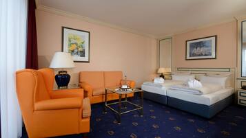 A hotel room with an orange armchair, a sofa, a bed, a small table, and a nightstand.