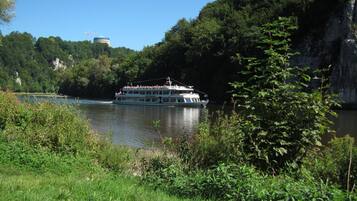 Un barco de crucero fluvial con exterior blanco y varias cubiertas, rodeado de vegetación exuberante y un acantilado rocoso.