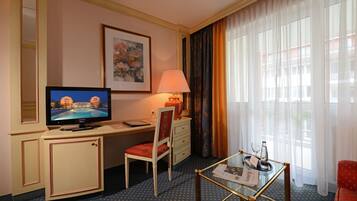 Ein Hotelzimmer mit Fernseher, Schreibtisch, Stuhl und einem kleinen Tisch mit Glasplatte.