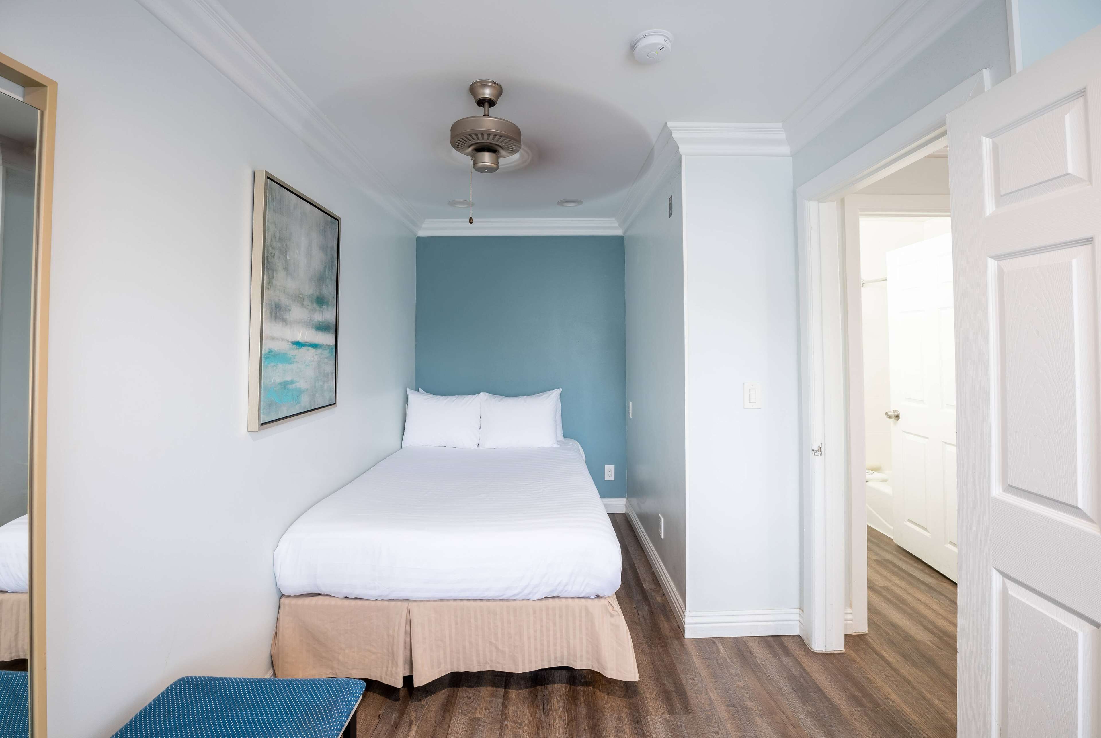A bedroom with a bed, a ceiling fan, and a door leading to another room.