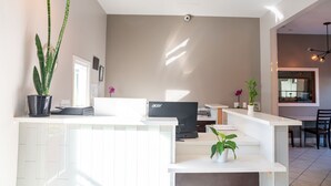 A modern living room with a white reception desk, a flat-screen TV, and a dining area with a table and chairs. - Ramada Limited Redondo Beach (Redondo Beach)