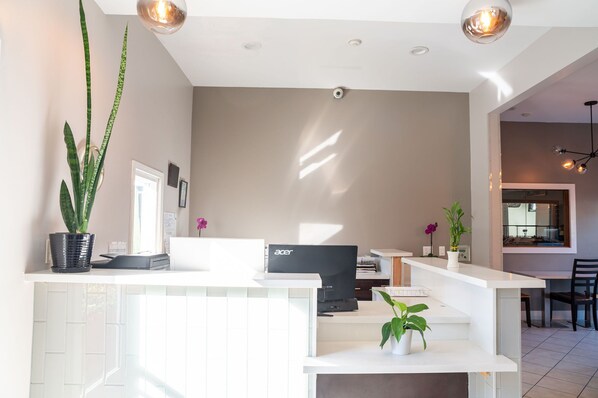 A modern living room with a white reception desk, a flat-screen TV, and a dining area with a table and chairs. - Ramada Limited Redondo Beach (Redondo Beach)