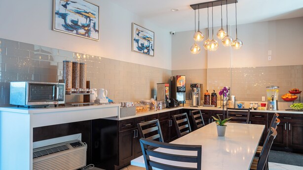 A modern kitchen with a central island, dark cabinetry, and a dining area with a white table and chairs. - Ramada Limited Redondo Beach (Redondo Beach)