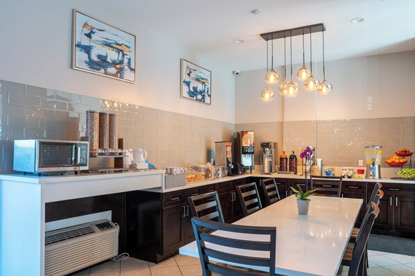 A modern kitchen with a central island, dark cabinetry, and a dining area with a white table and chairs. - Ramada Limited Redondo Beach (Redondo Beach)
