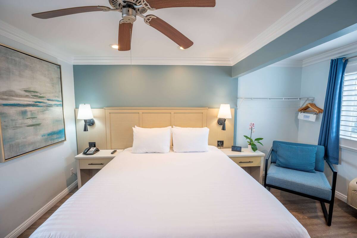 Habitación de hotel con cama, escritorio, silla, ventilador de techo y lámpara de pared.