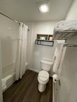 Un baño con ducha, inodoro y estante con artículos de aseo.
