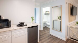 A compact kitchen with a microwave, coffee maker, and dishwasher. A large mirror and a flat-screen TV are mounted on the wall. - Ramada Limited Redondo Beach (Redondo Beach)
