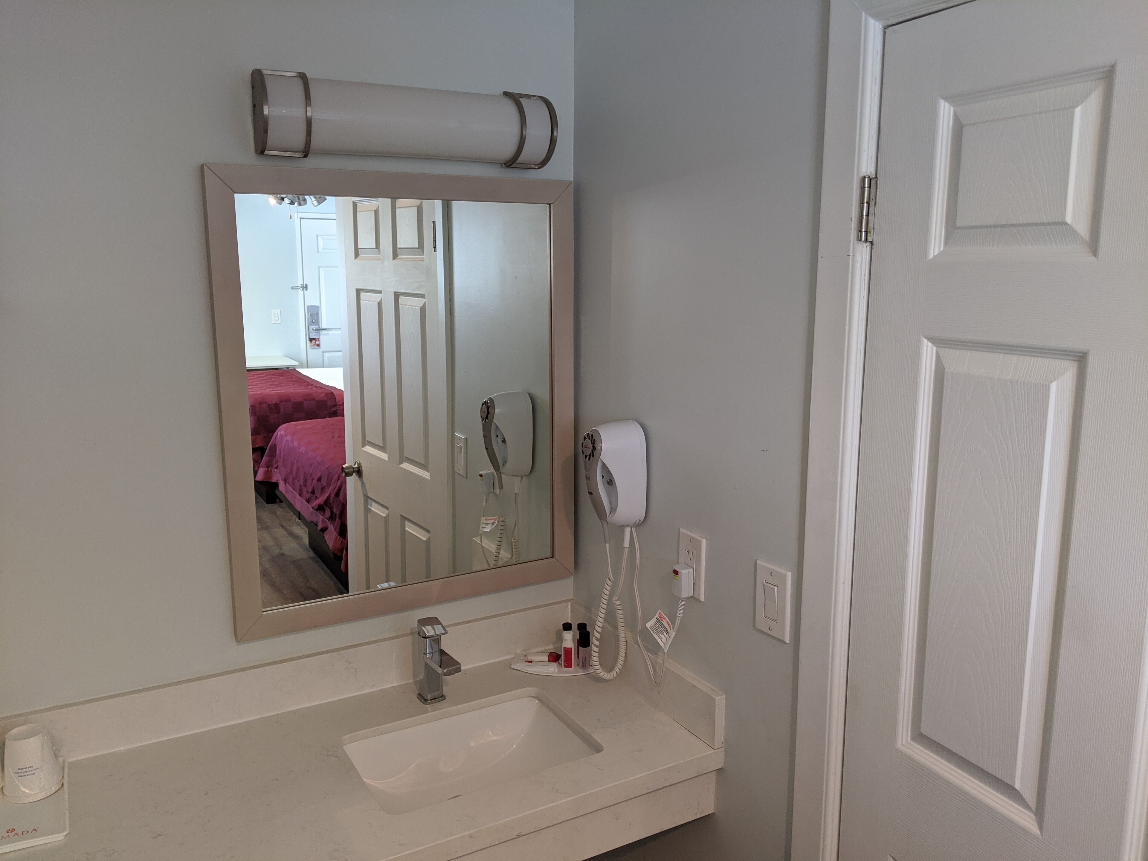 A bathroom with a sink, mirror, and two hair dryers mounted on the wall.