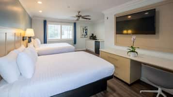 A hotel room with two beds, a desk, a chair, a TV, and a ceiling fan.