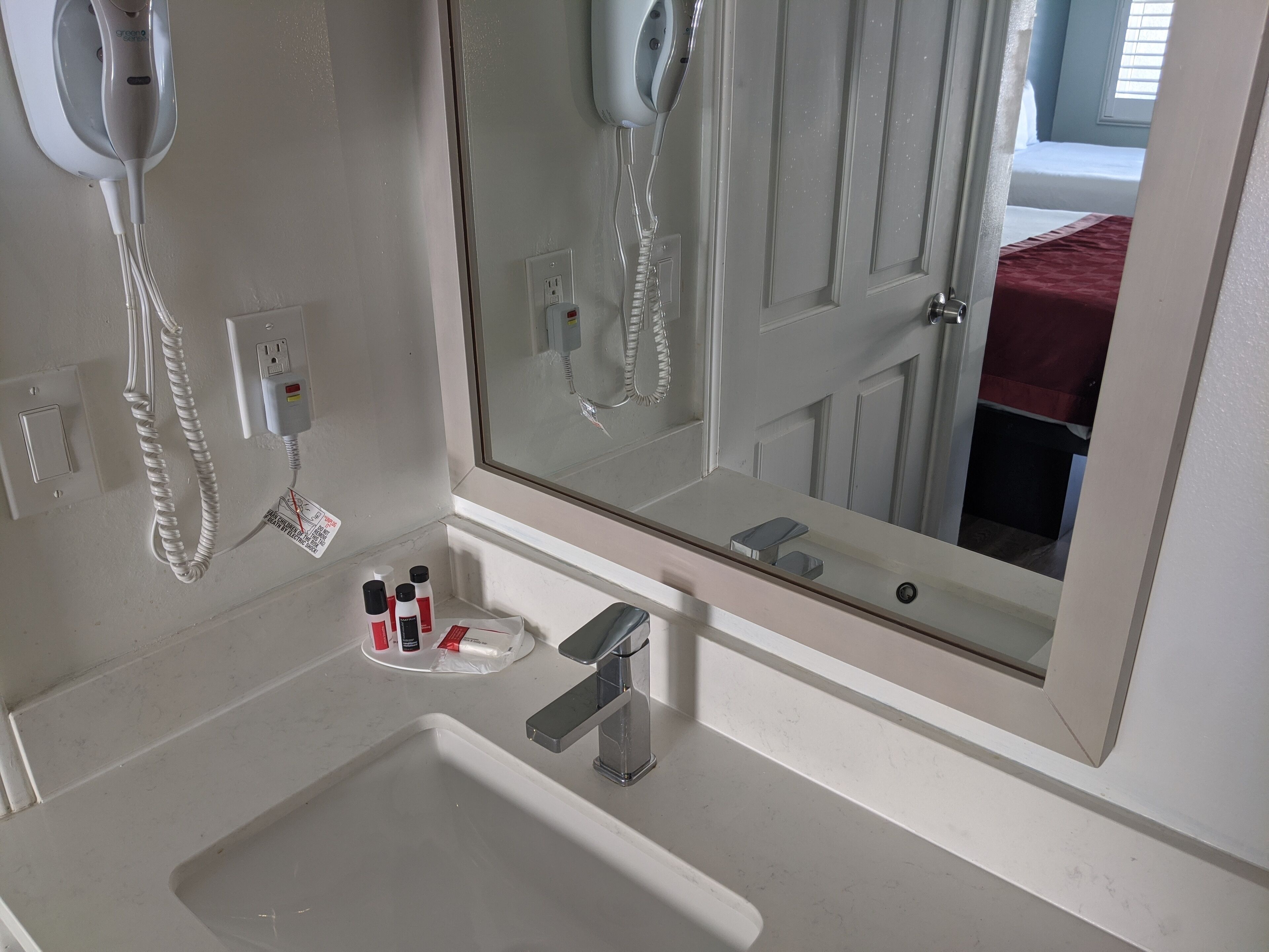 A bathroom with a white sink, a mirror, a hairdryer, and a few toiletries on the counter.