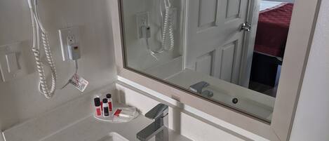 A bathroom with a white sink, a mirror, a hairdryer, and a few toiletries on the counter.